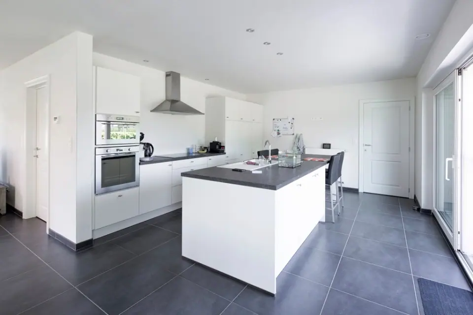 A white kitchen with a freestanding island and dark tiled floor
