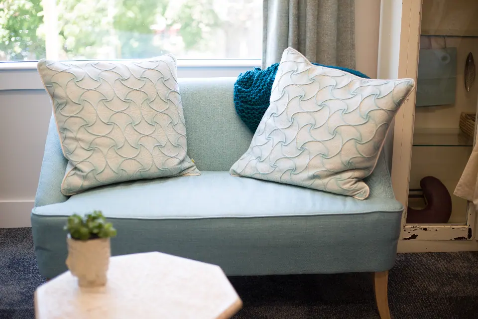 A pale sofa with cushions beside a large window with a garden beyond